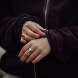Detailaufnahme der Fleecejacke VARM in Chocolate Braun: Hände mit Ringen greifen an den weichen Ärmelbund, der dank Gummizeug individuell verstellbar ist. Die Jacke besteht aus 100 % Baumwolle, gefertigt in Portugal.