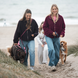 Fleecejacke VARM in Burgunder und Chocolate Brown von Hej Nika aus 100% Baumwolle, gefertigt in Portugal. Hej Nika Stick auf der Brust. Durch Gummizug einstellbare Ärmel und Bund. Frauen beim Hundespaziergang in den Dünen am Strand.