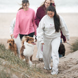 Frauen am Strand, im Vordergrund das graue Jogger-Set von Hej Nika aus Baumwolle und recyceltem Polyester. Gefertigt in Portugal. Kuschelig weich mit Print in Burgunder auf der Vorderseite.