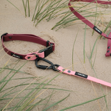 BioThane® Umhängeleine Mérida DUO in Red Wine / Rose mit schwarzem Sicherheitskarabiner und passendem Halsband, liegend im Sand zwischen Dünengras.