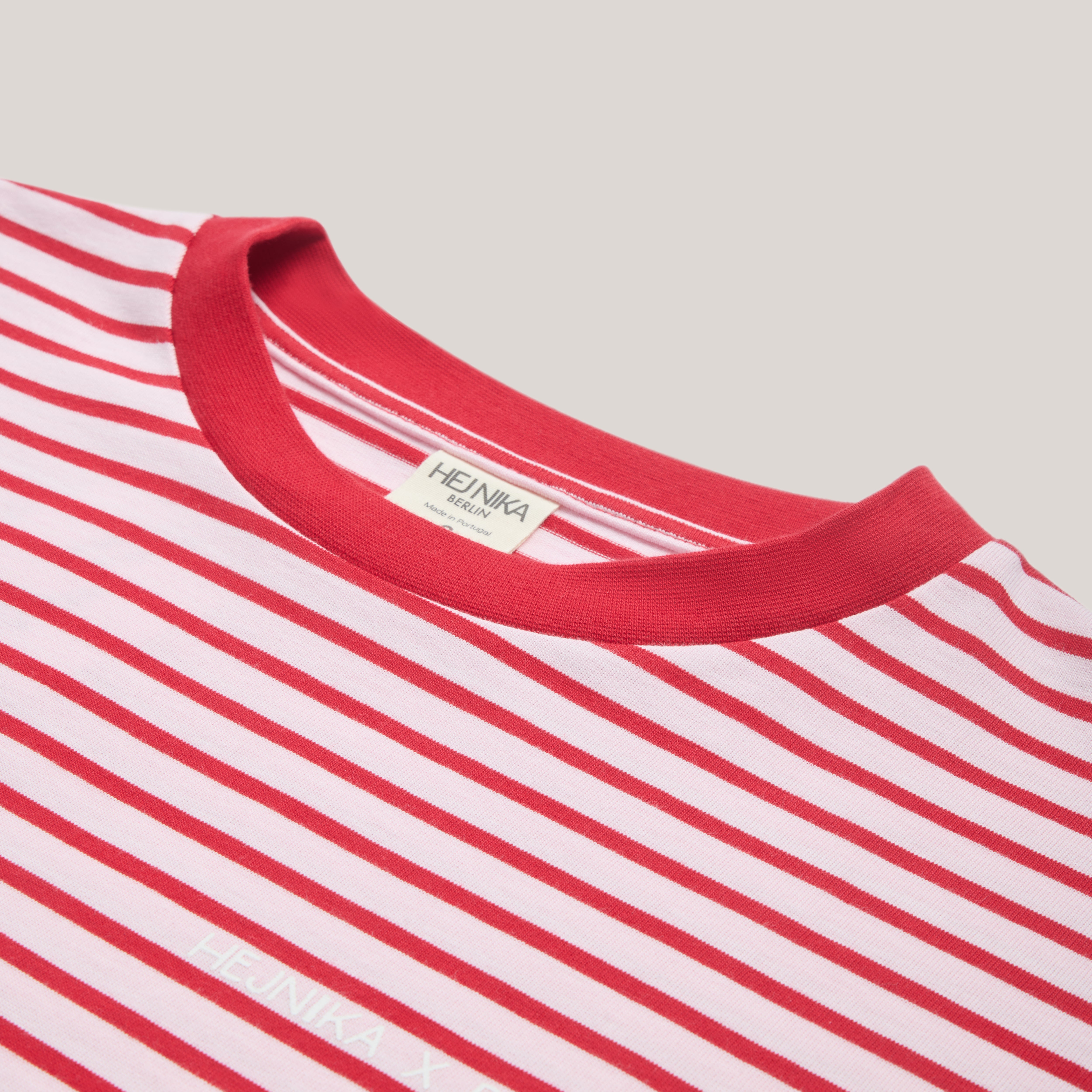 Detailaufnahme des roten Rundhals-Kragens (Crewneck) und des Hej Nika Nackenlabels am gestreiften Longsleeve.