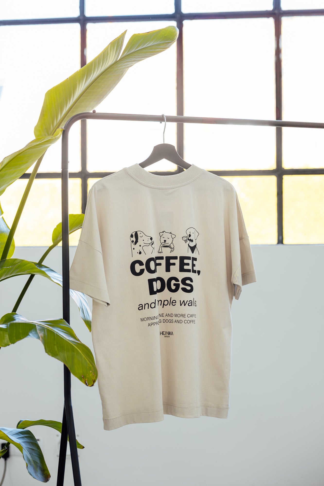 COFFEE & DOGS T-Shirt hängt drapiert an Kleiderstange – sanfter Moonbeam Ton – Hej Nika