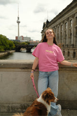 Frau kombiniert das pinke Hej Nika Dog Girls T-Shirt mit heller Jeans und hält einen braun-weißen Hund an der Leine