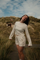 Frau trägt das creme-beige gestreifte Hej Nika Longsleeve mit passender Shorts in einer sommerlichen Dünenlandschaft