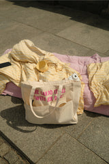 Cremefarbener Hej Nika Shopper mit pinkem „She Can Do It All With Her Dog“-Schriftzug auf einer gelben Picknickdecke im Sonnenlicht.