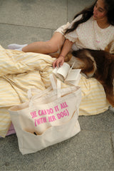 Cremefarbener Hej Nika Shopper mit pinkem Statement-Print neben einer Frau und ihrem Hund auf einer gelben Picknickdecke.