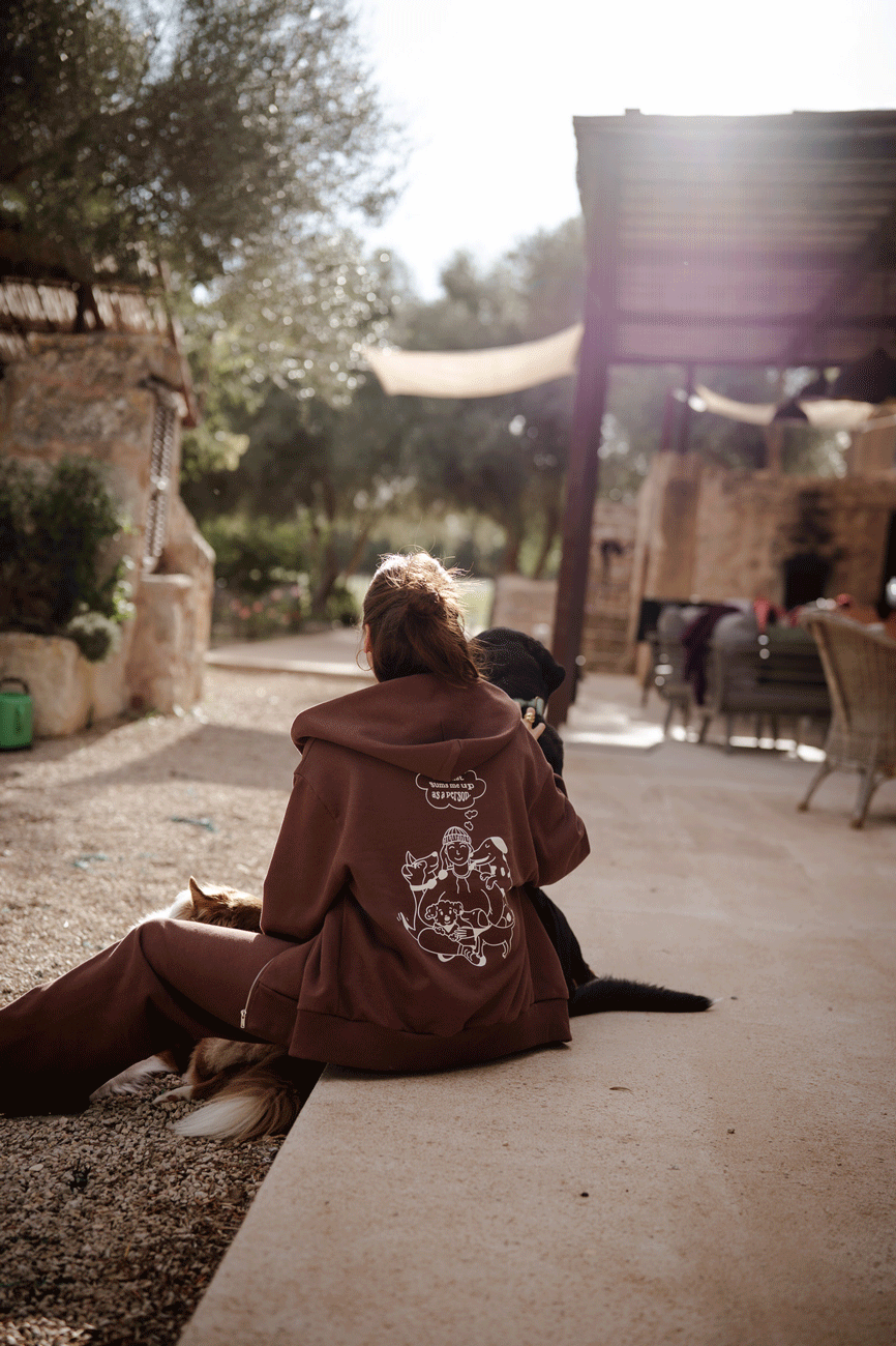 Hundebesitzer trägt Unisex Sweatjacke in Braun beim gemeinsamen entspannen mit Hund im garten.